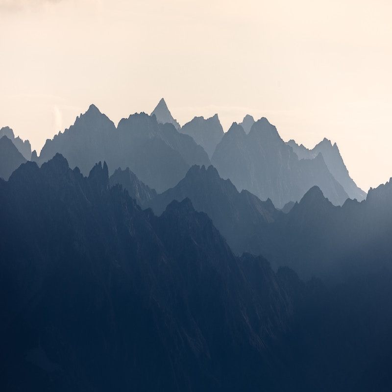 Silhouetted mountain peaks layered in the distance under a hazy, pale sky, creating a serene and atmospheric landscape.