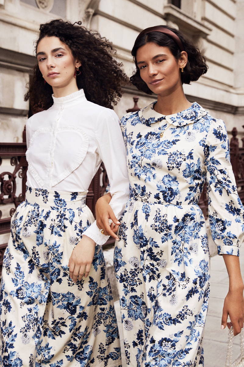 Two friends walk arm in arm down the streets of London wearing YOLKE's matching cotton prairie skirt and Ophelia Dress in the Ditsy Denim Print