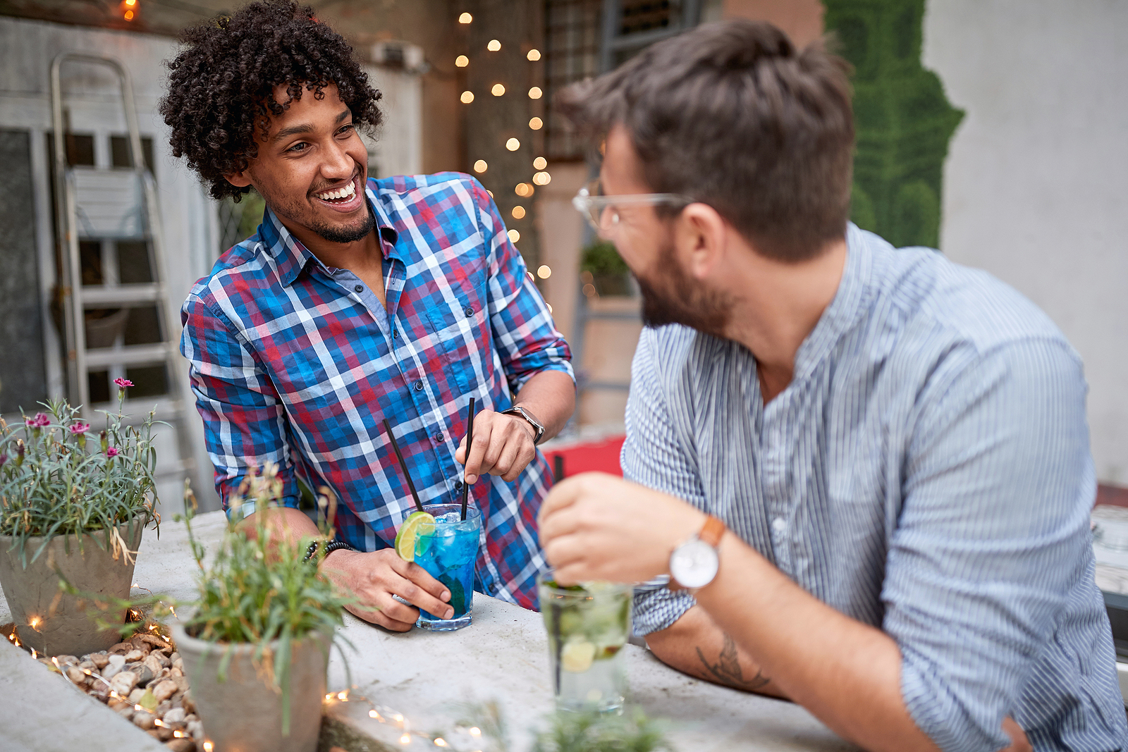 Two multi racial men laugh together while having  a drink at a house.