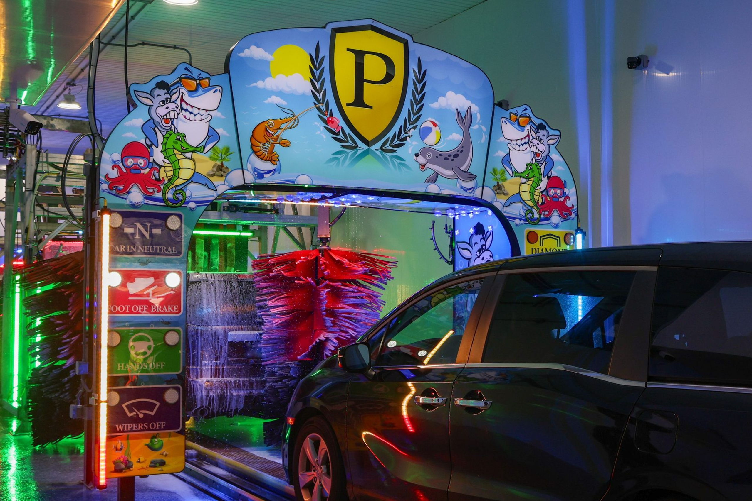 The entrance of a Prestige tunnel: a minivan rolling in under the lit arch and the mural of the P shield, the soft-cloth brushes turning ahead