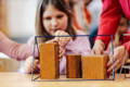 Little girl playing wooden geometric shapes in classroom.
