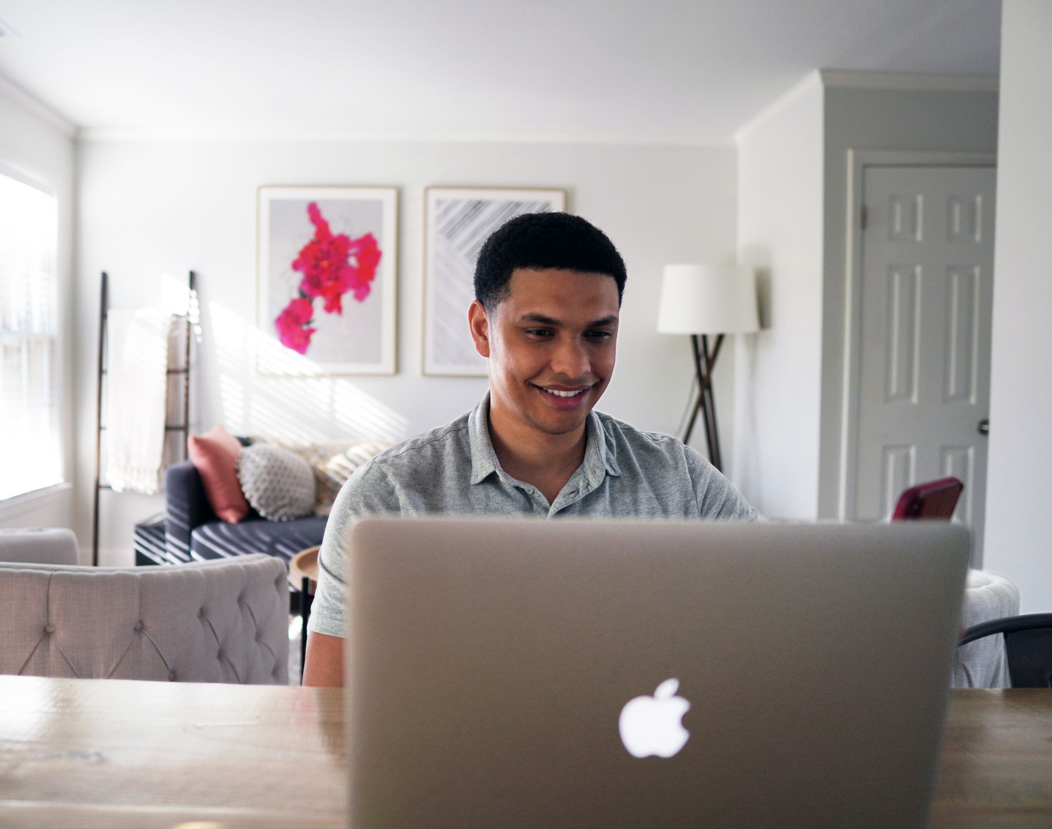 An attractive multi ethnic man smiles while looking at his laptop. He is at his sunny home.