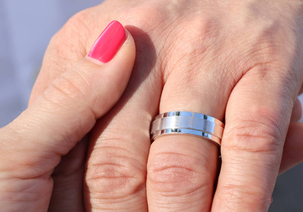 A woman's hand with red nail polish holds the hand of a man wearing an engagement ring on his ring finger.