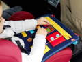 A little girl playing with the Busy Board in the back seat of a car while on a trip. 