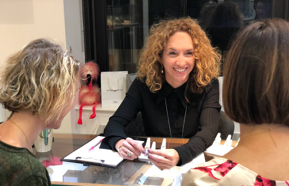 A pretty jeweler sitting at an appointment counter advises two women sitting across from her on a transformation.