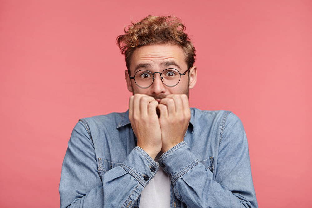 Man in glasses biting his fingernails