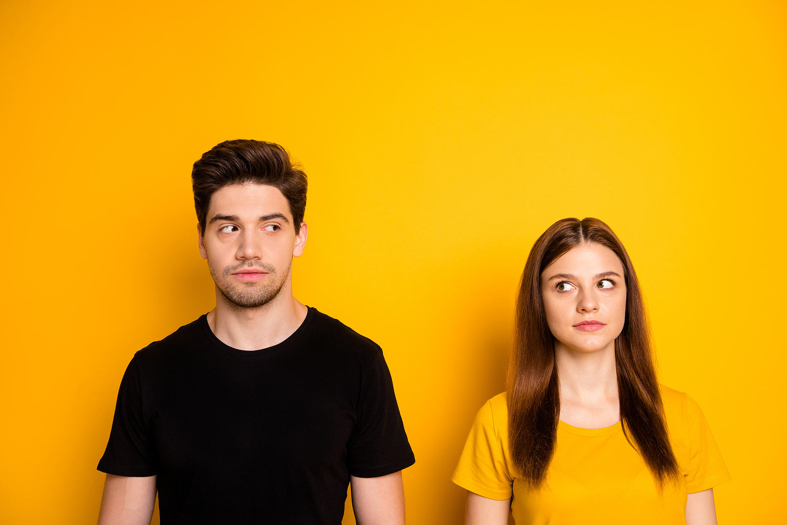 A young man and a woman both look at eachother standing side by side with a curious expression.