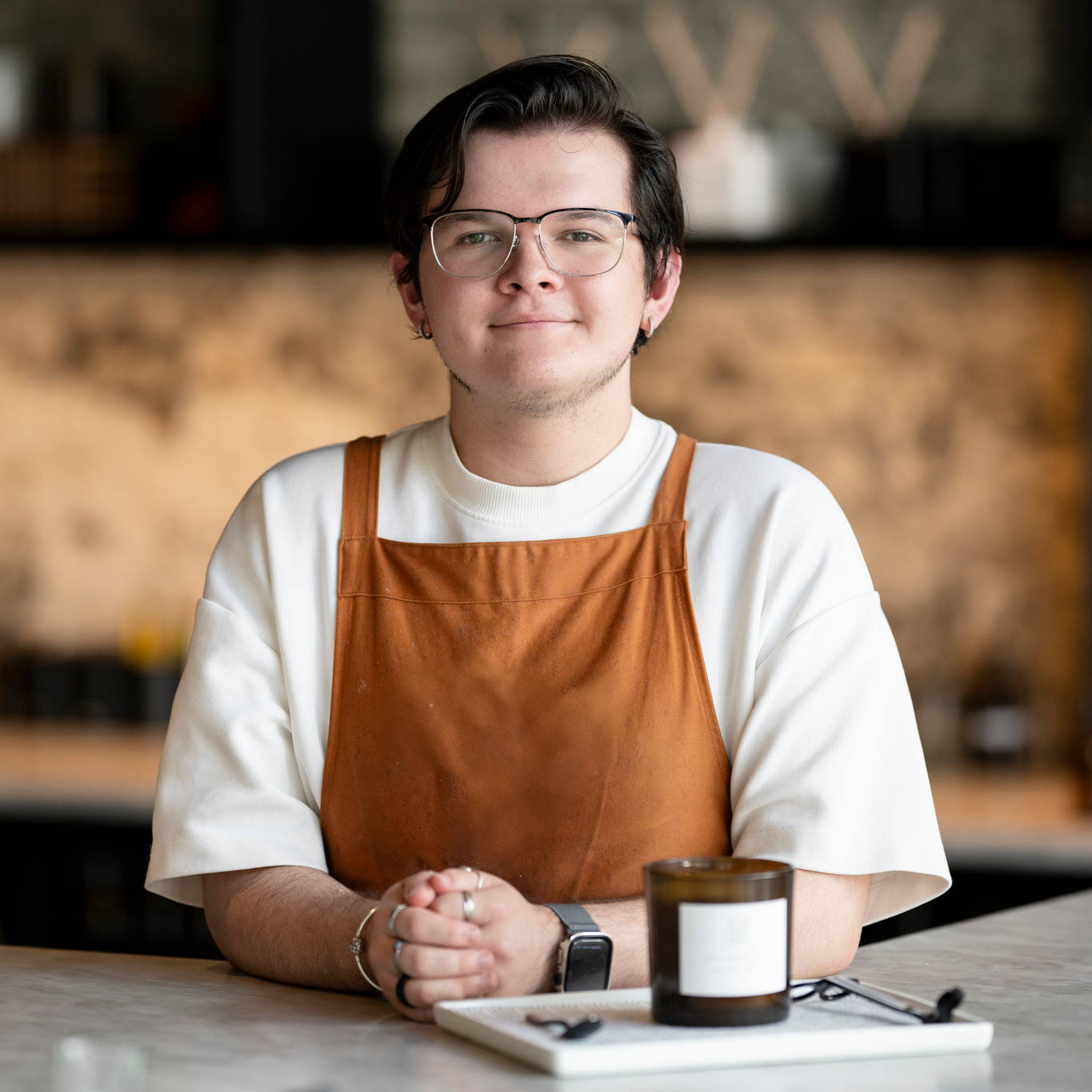 male in orange apron in front of candle