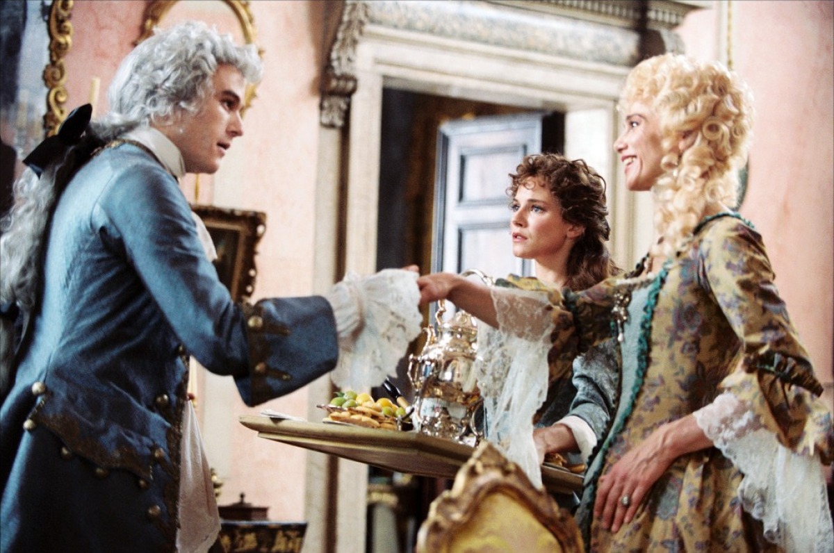 Casanova dressed in the old school victorian clothing, has his hand out for a pair of women smiling at him.