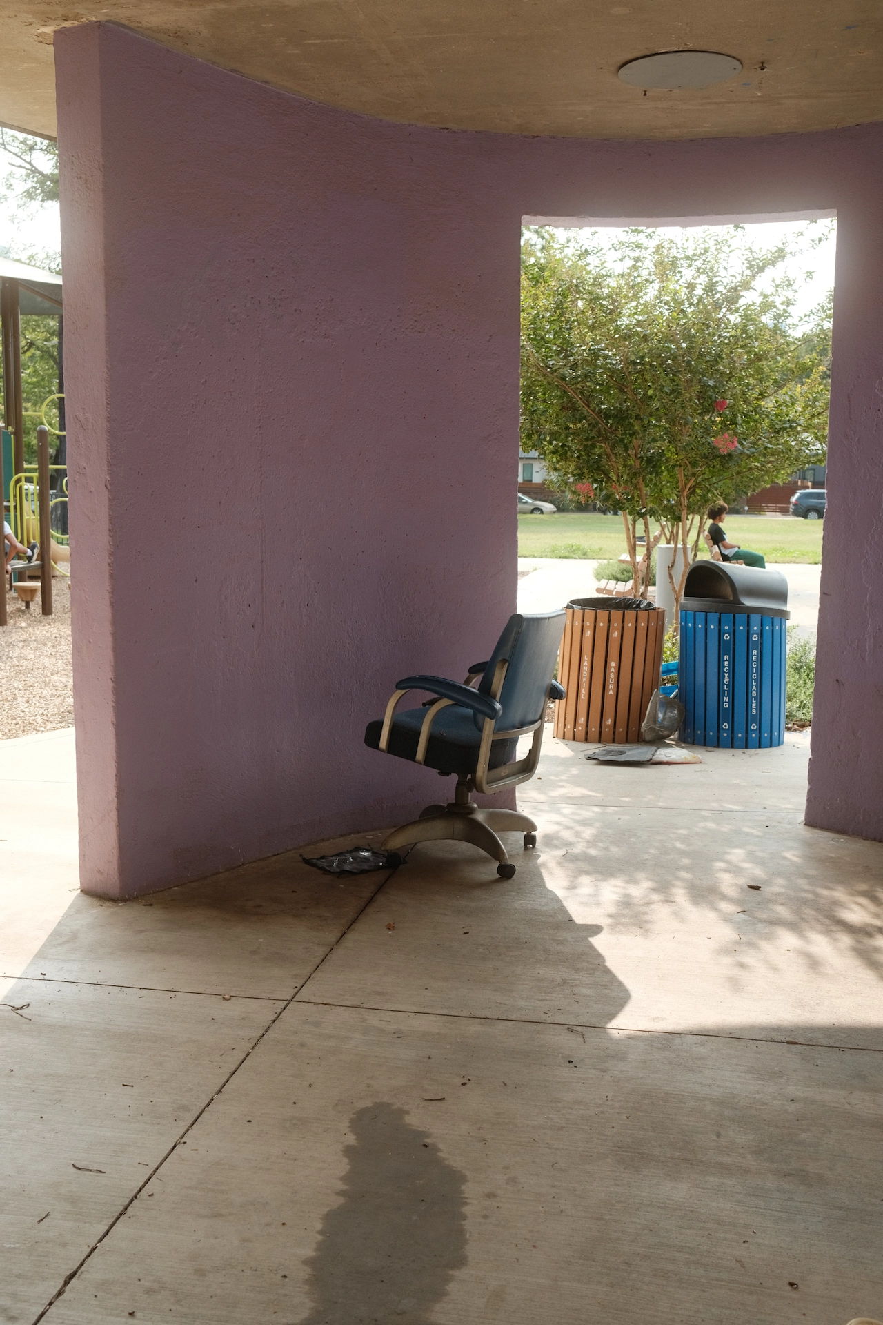 empty metal chair sits on a sidewalk near a colorful mural, with sunlight casting soft shadows and a relaxed, quiet atmosphere
