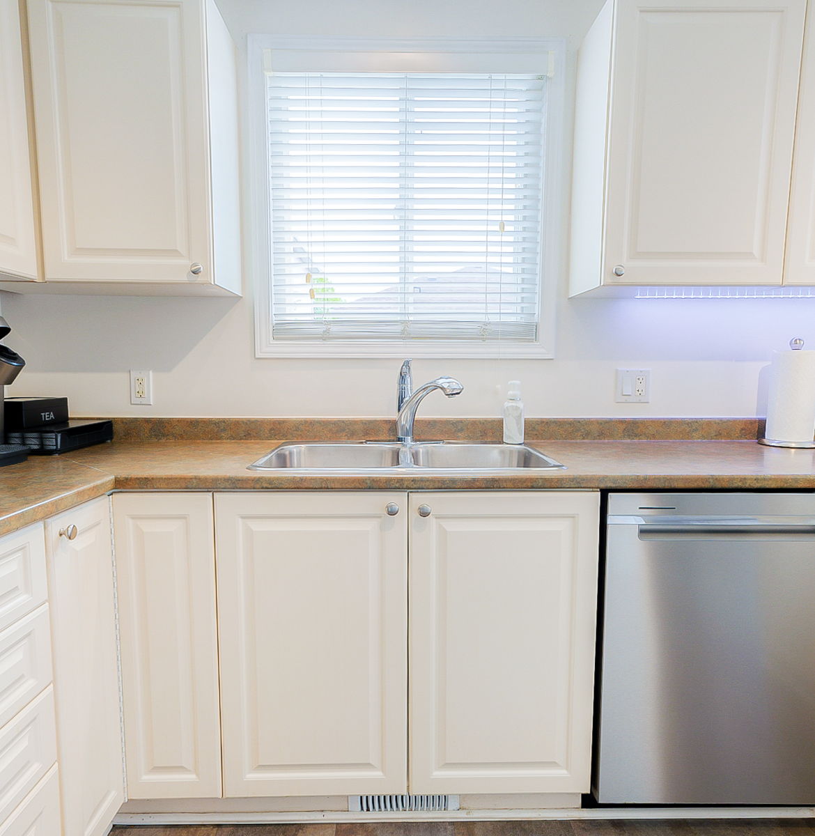 kitchen with natural light, stainless steel dishwasher, white cabinets, and light countertops