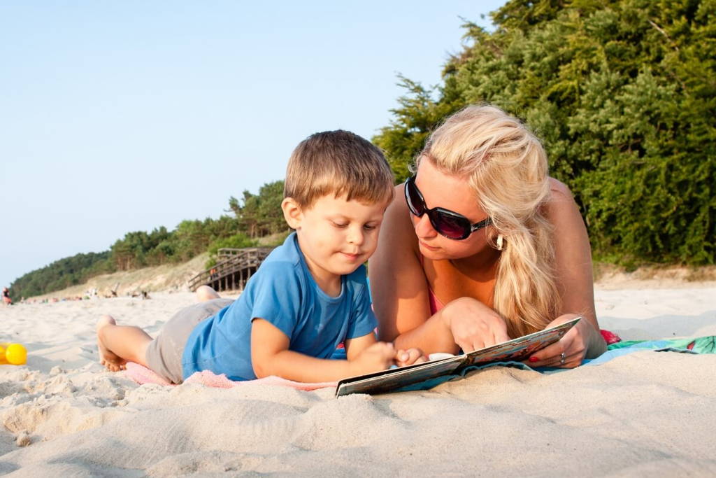Mother and son reading a book at the beach.