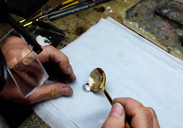 Une joaillière introduit des cendres dans une cavité de bijou.