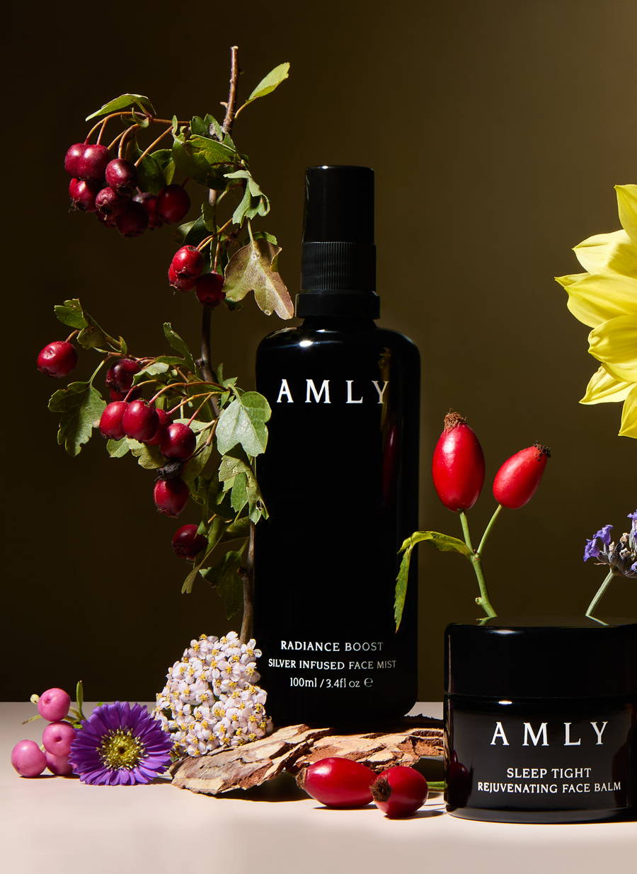 AMLY products surrounded by berries, seeds and flowers with a dark yellow background