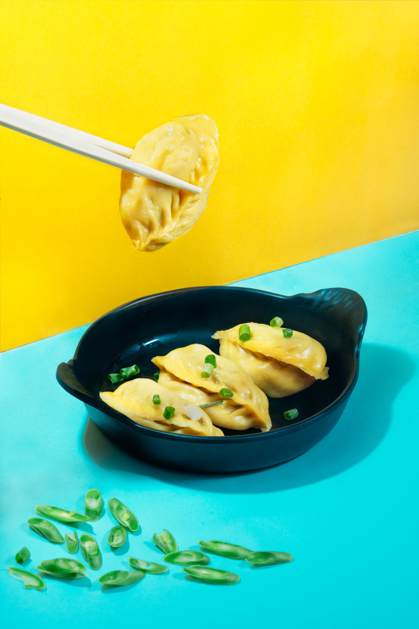 A close-up of a plate of jiaozi dumplings with chopsticks and green onions on a blue table