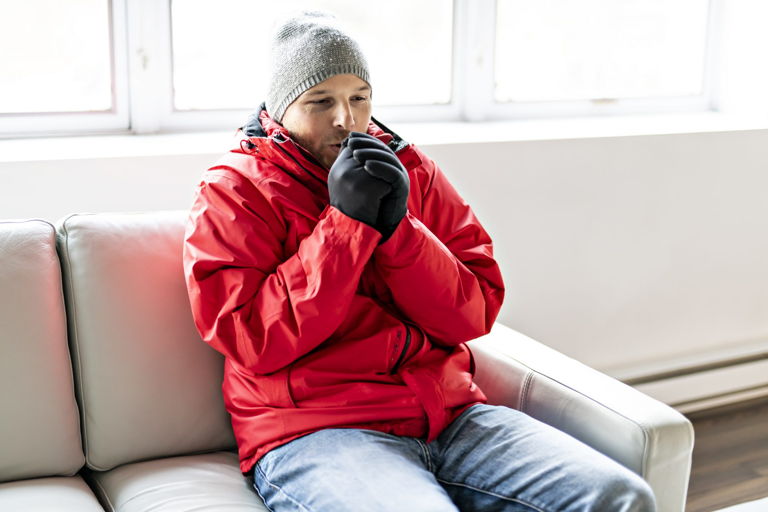 a man sitting on a couch trying to keep warm