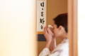 A women drinking matcha in kimono. A calligraphy scroll on the wall.