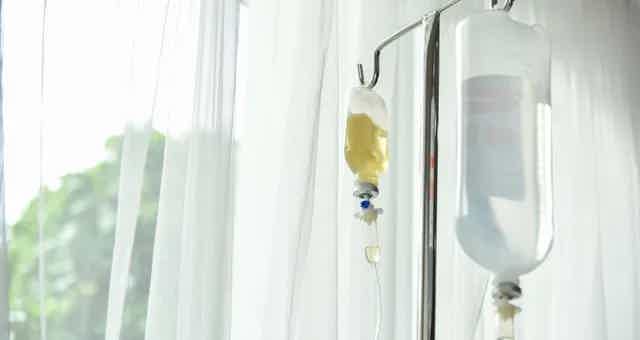 IV drip bag with yellow fluid and tubing attached to a stand beside a window.