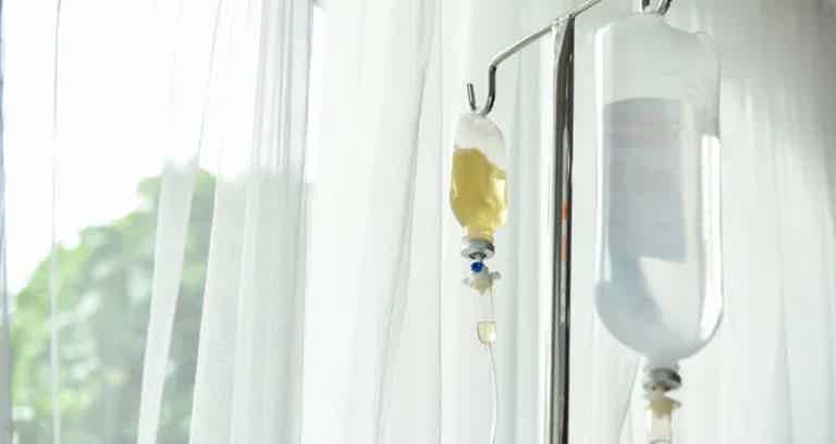 IV drip bag with yellow fluid and tubing attached to a stand beside a window.