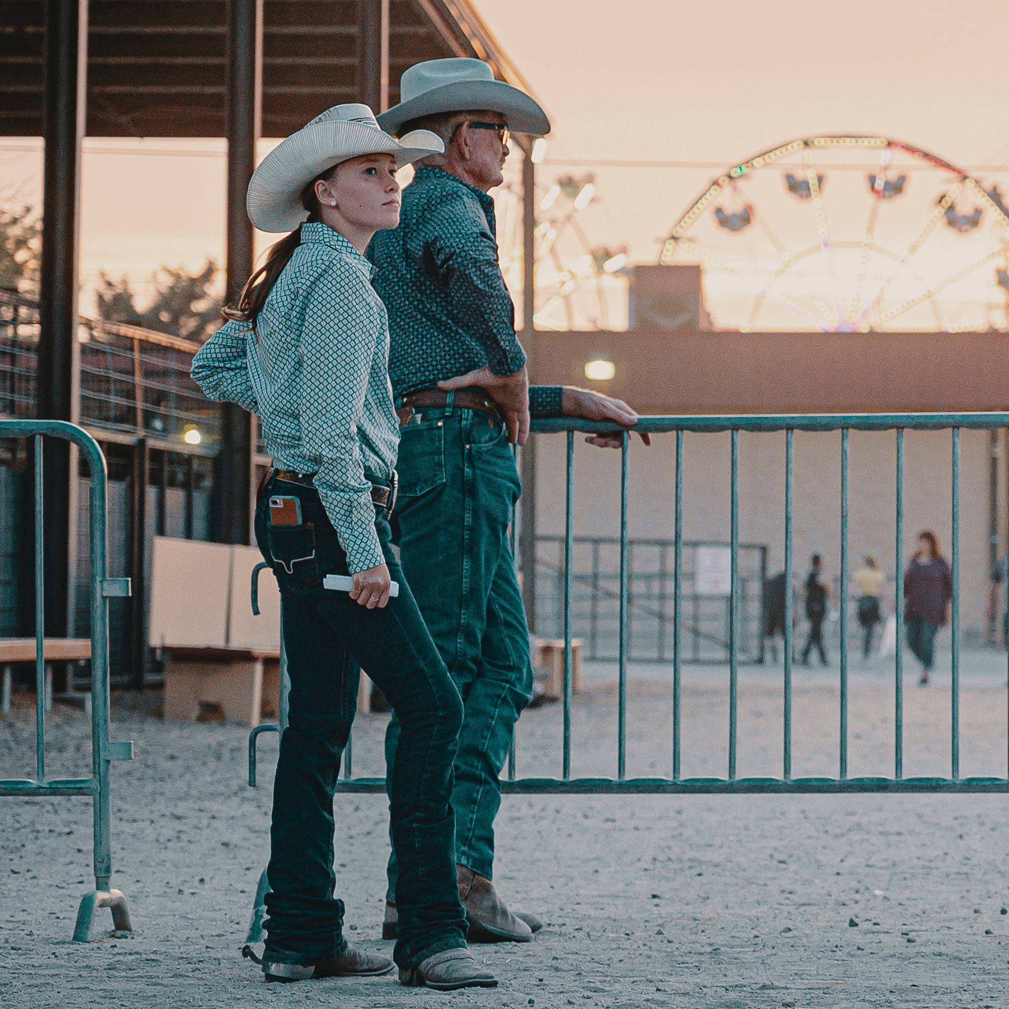 Image of 2 people dressed in cowboy hats, button up shirts, jeans, and cowboy boots