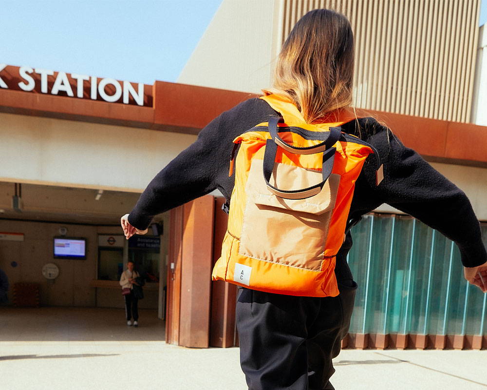 Model wears Harry Packable Zip Top Tote/Backpack in Orange