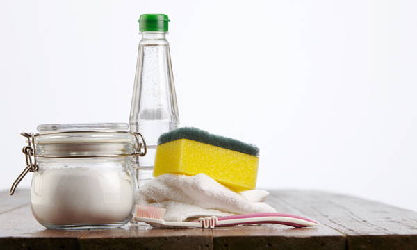 Jar of vinegar, baking soda on a table with a toothbrush and cloth.