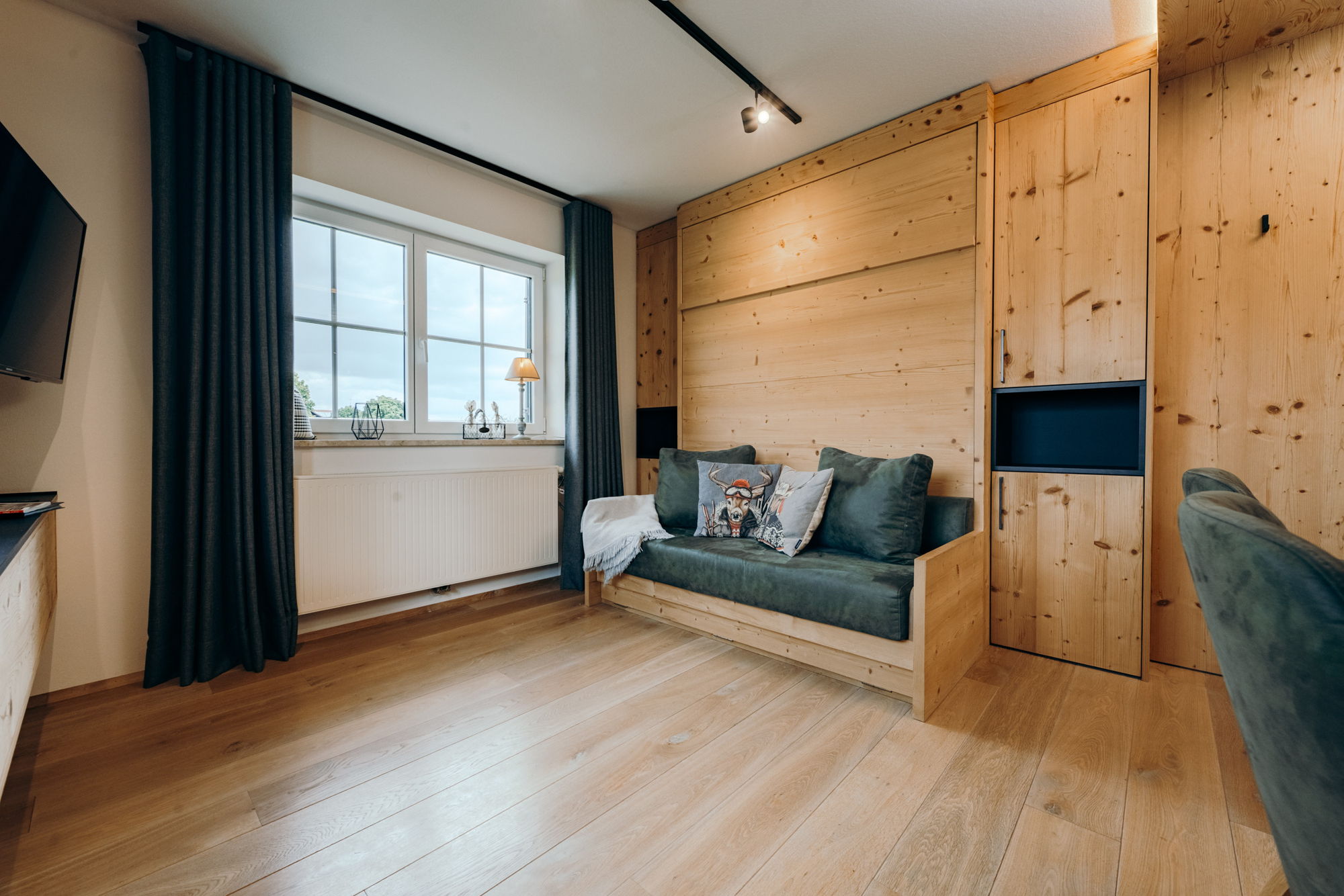 Ein graues Sofa mit Hirschkissen in einem modernen, hölzernen Wohnzimmer.