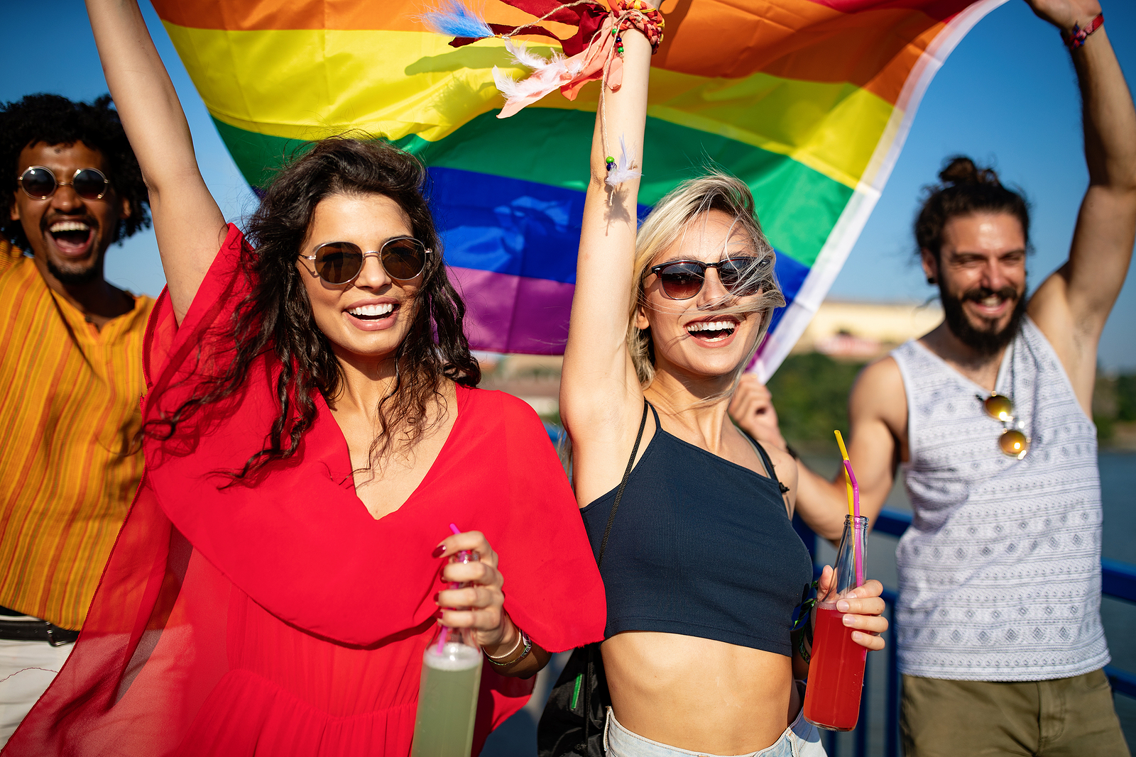 An ethnically diverse group smiling walking together and holding a rainbow flag.