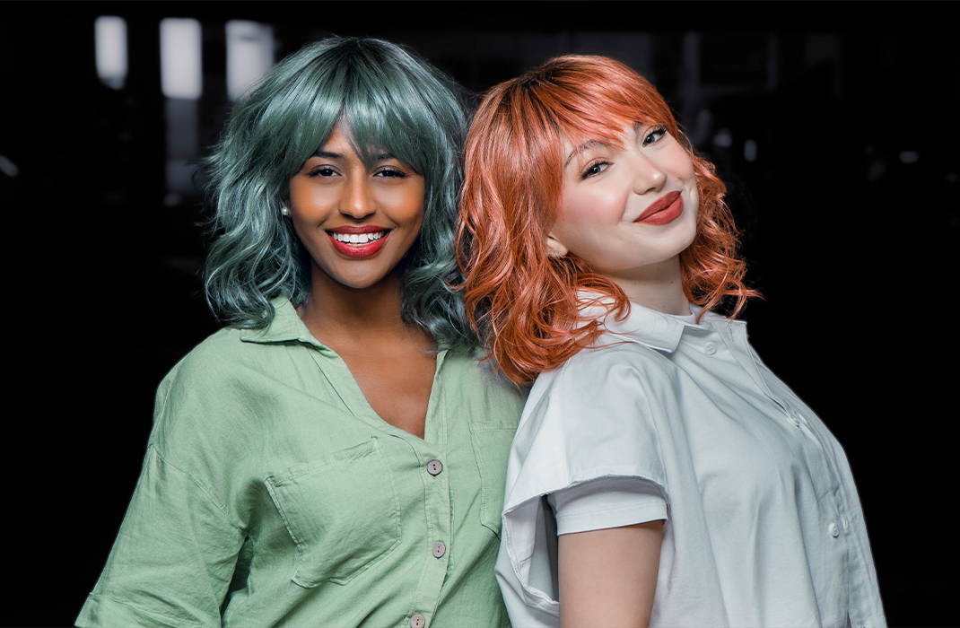 Two women (Maha and Sophia)  wearing wigs in the style Breezy Wavez by Rene of Paris in shades Smoky Forest and Dusty-Rose are standing next to each other.