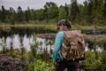 woman walking next to a small lake in the woods wearing an isle royale pack