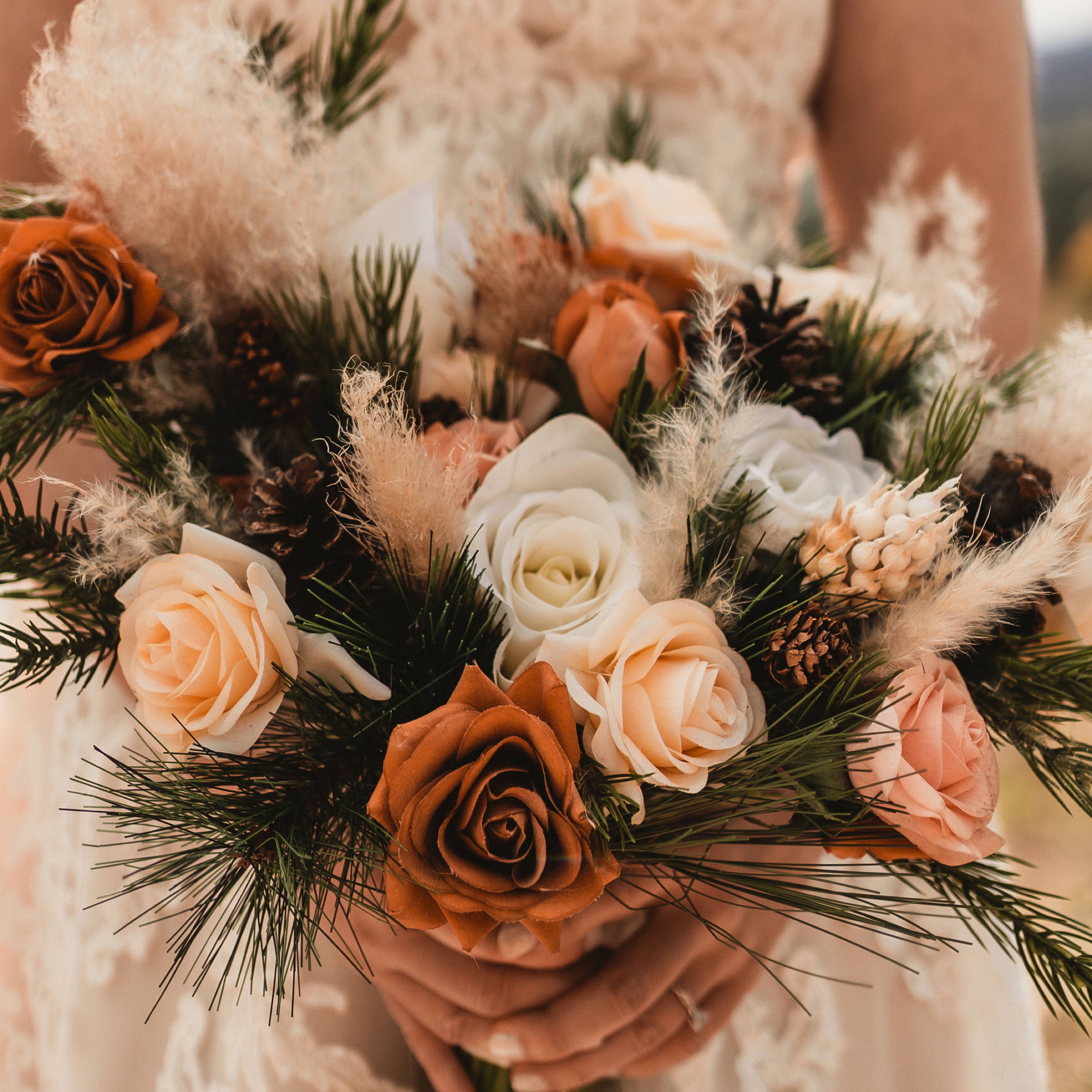 Unique bridal bouquet with pampas grass, pine, pine cones, and rust, peach, and white roses 