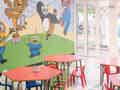 Ein heller, bunter Kinderspielbereich mit Wandmalereien, kleinen Tischen und großen Fenstertüren.
