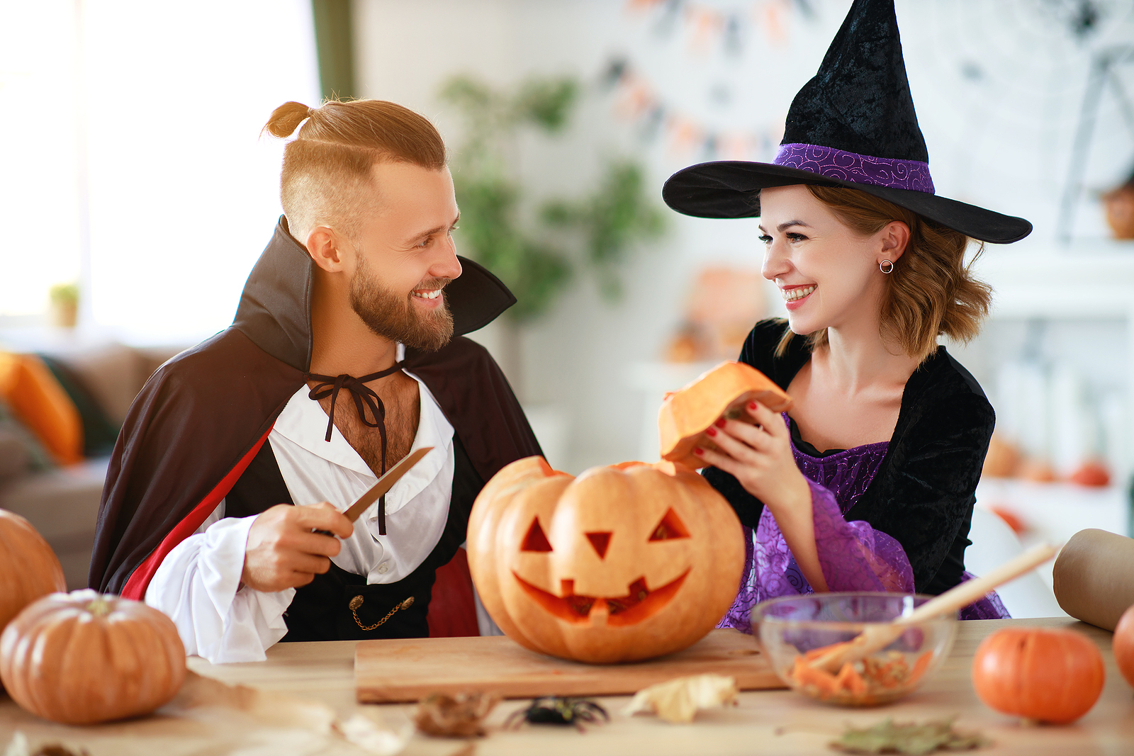 couple of people are preparing for Halloween in costumes of a witch and a vampire with pumpkins