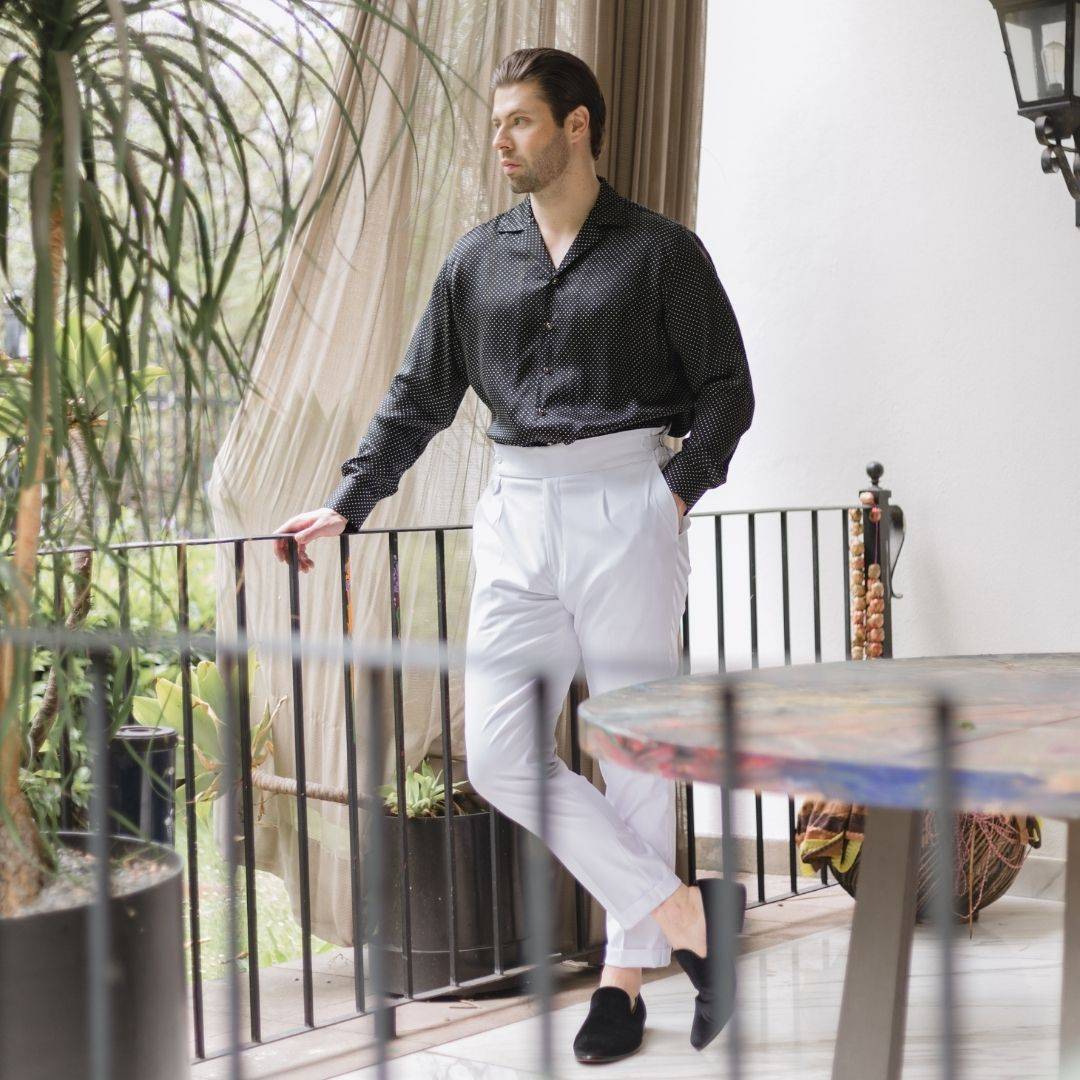 model standing outside wearing black velvet shoes white pants and a long sleeve black dotted silk shirt from 1000 kingdoms