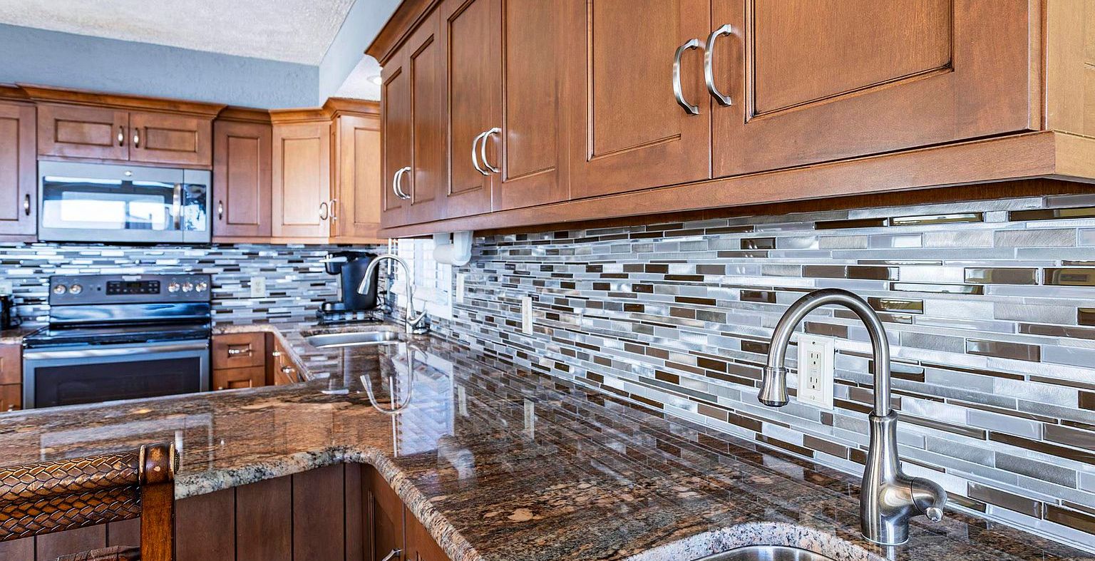 kitchen with dark stone counters, stainless steel appliances, backsplash, and brown cabinets