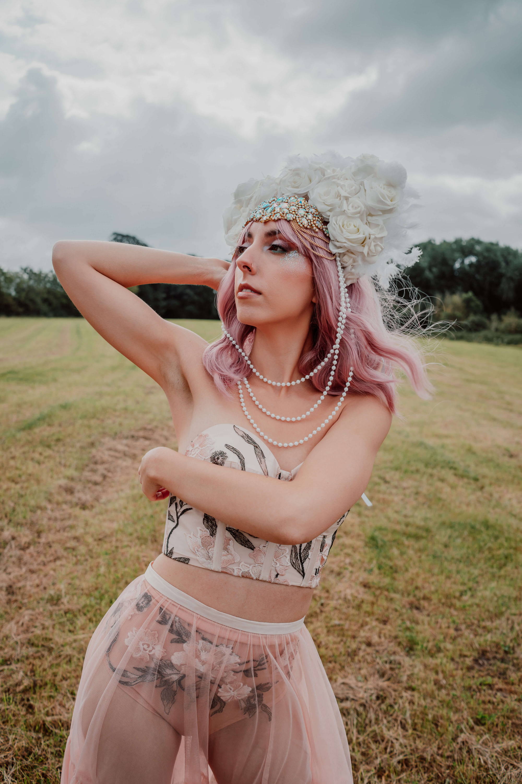Image of a bride at a festival. She is wearing an embroidered modern bridal outfit, white head piece instead of a veil, and has biodegradable blue, pink, and iridescent glitter on her face.