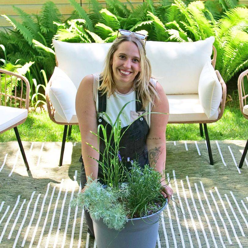 Blonde woman posing next to patio container full of plants