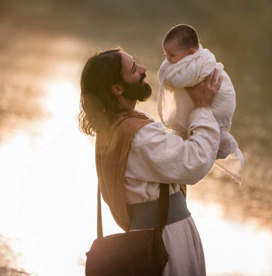 Jesus is smiling as He lifts and infant up to HIs face.