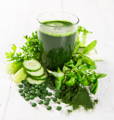a tall glass of green wheat grass juice surrounded by green vegetables