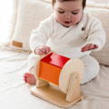 Baby sitting on a sofa and playing with a Montessori Spinning Drum wooden toy.