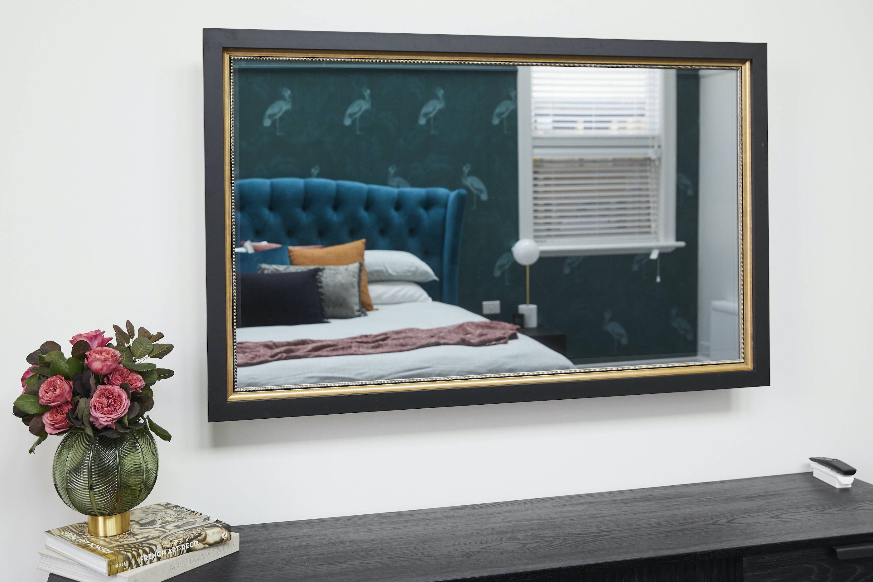 A close up TV-Mirror in a bedroom, reflecting a patterned wallpaper and velvet bedhead 