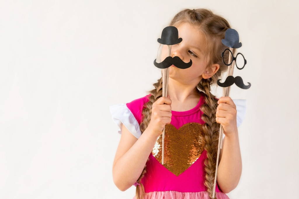 Little girl posing with pretend play sticks with mustaches.