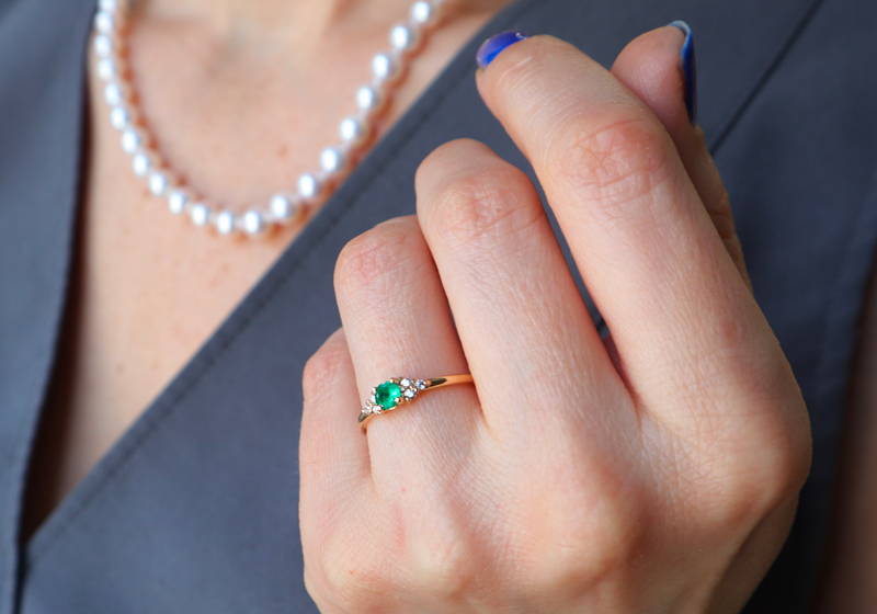 Ring with an emerald on a hand folded near a woman's chest. 