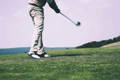 Golfer completing swing follow through after hitting golf ball on green grass field.