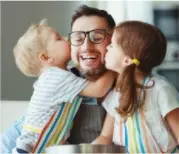 Man with glasses getting a kiss from his son and daughter while baking in the kitchen