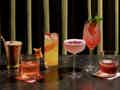Auswahl an farbenfrohen, garnierten Cocktails auf einer Marmorbar vor einem dunklen Vorhang.