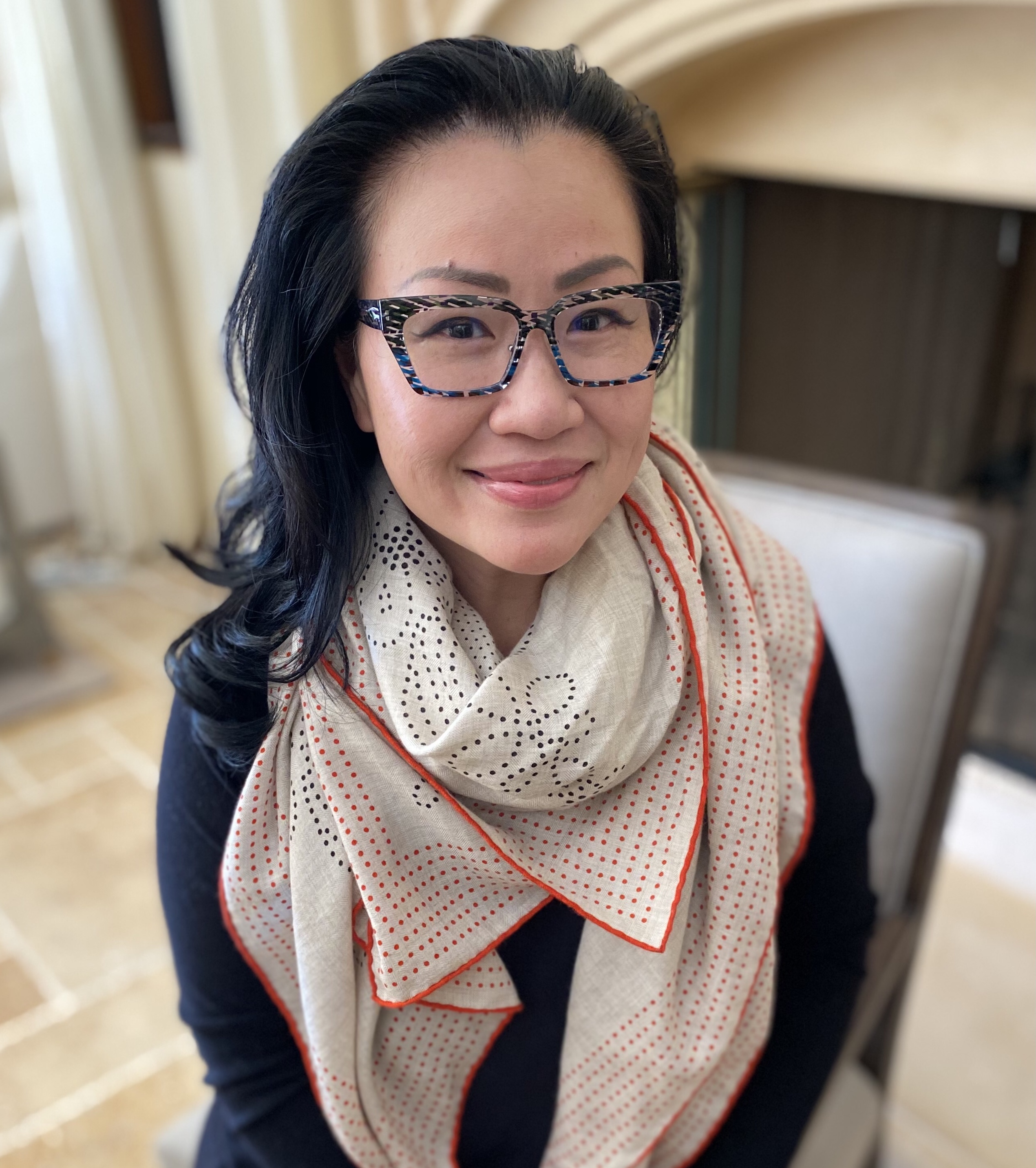 Winnie Koh wears a large scarf, patterned scarf and blue rimmed glasses at her home