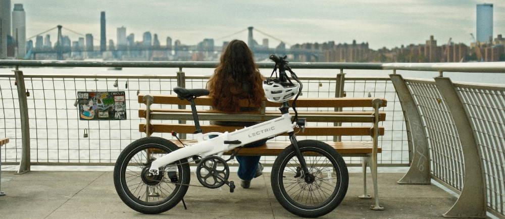 female looking over the water in NY with her ebike leaning on a bench