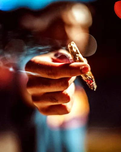 Artistic photo of a man handing the viewer a cannabis roach or joint