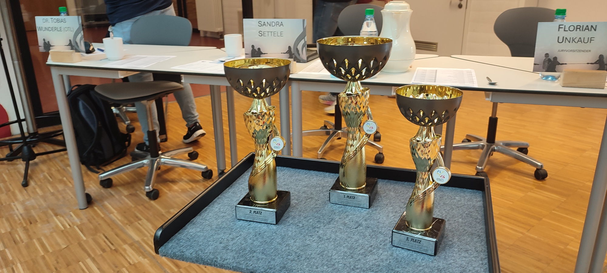 Drei goldene Pokale stehen nebeneinander auf einem Tisch. 